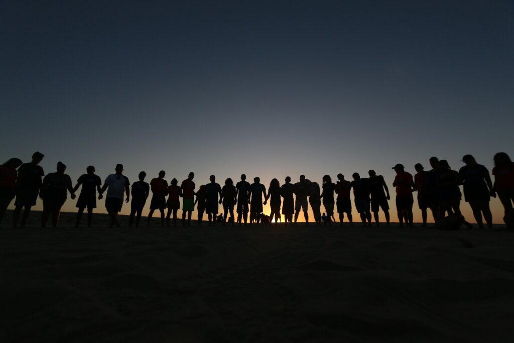 silhouettes of many people holding hands during sunset/sunrise