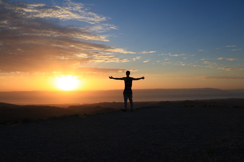 Person's silhouette with outreached arms at sunset